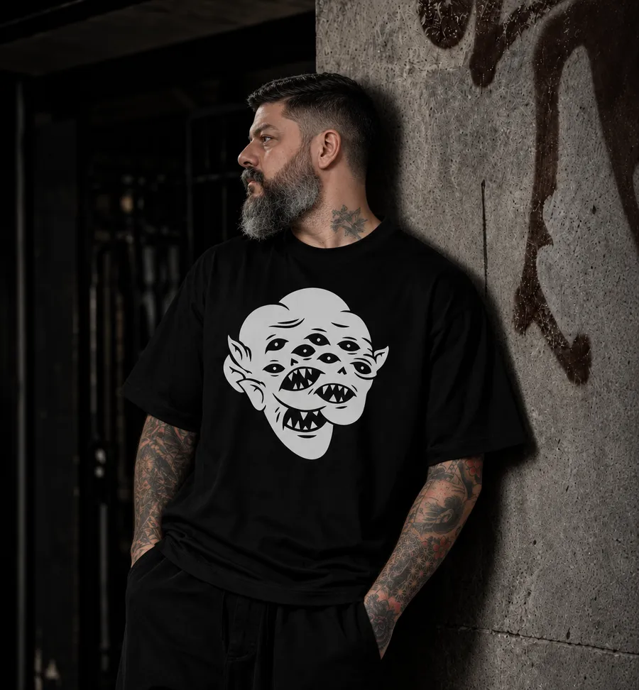 Black Monster T-shirt worn by a bearded, tattooed man leaning on a concrete wall