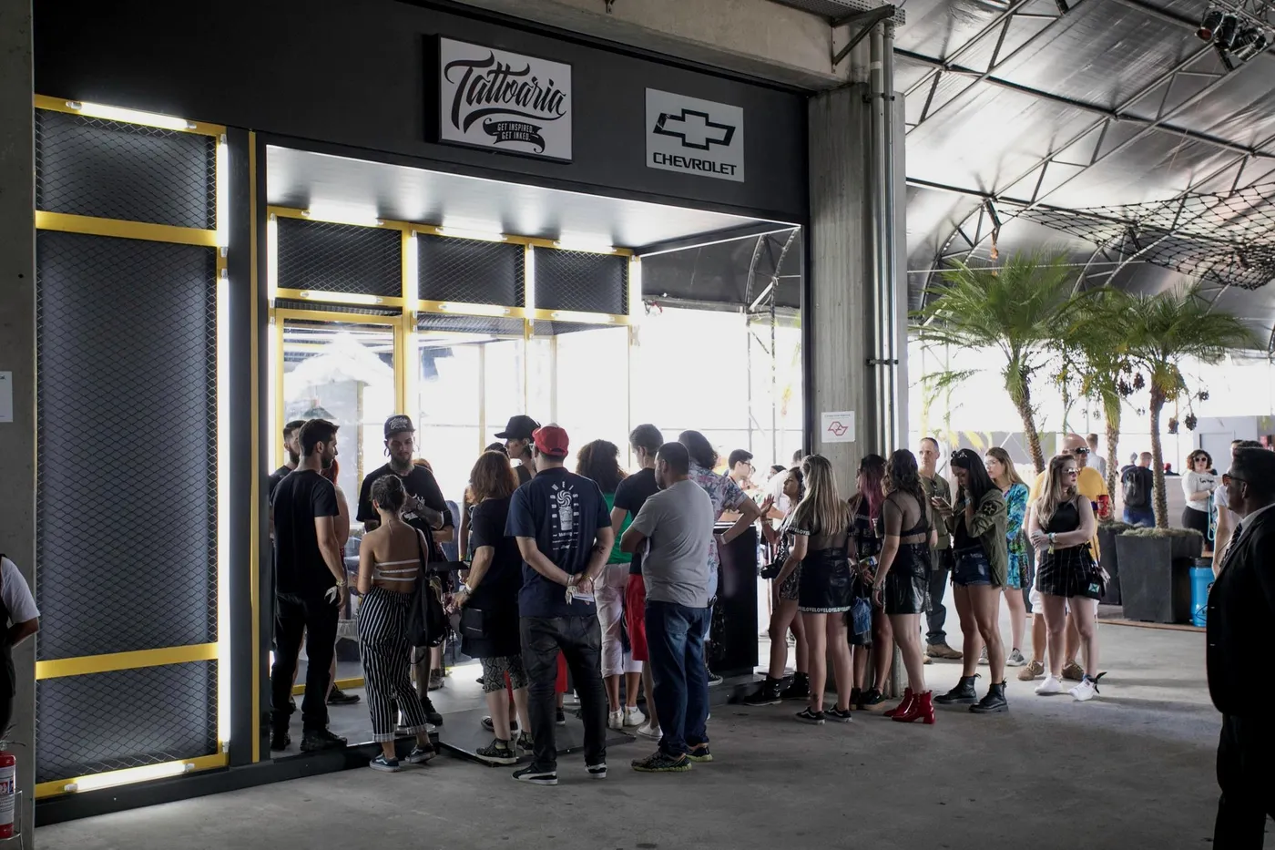 Fila na porta do estúdio da Tattoaria no Lollapalooza, com as placas da Tattoaria e da Chevrolet lado a lado.