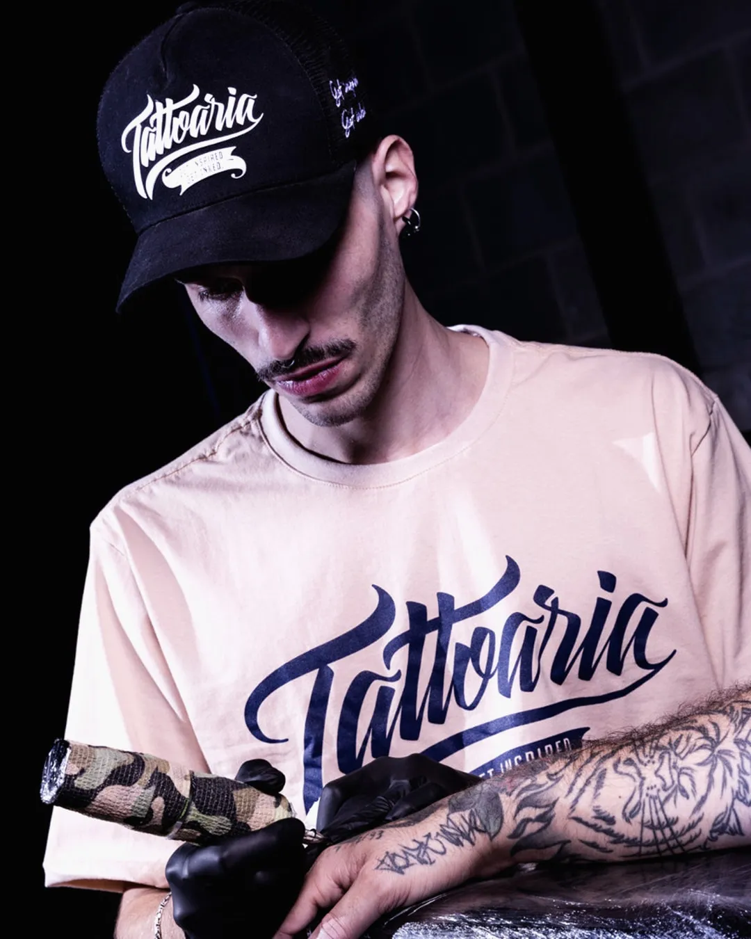Tatuador de boné e camiseta da Tattoaria trabalhando.